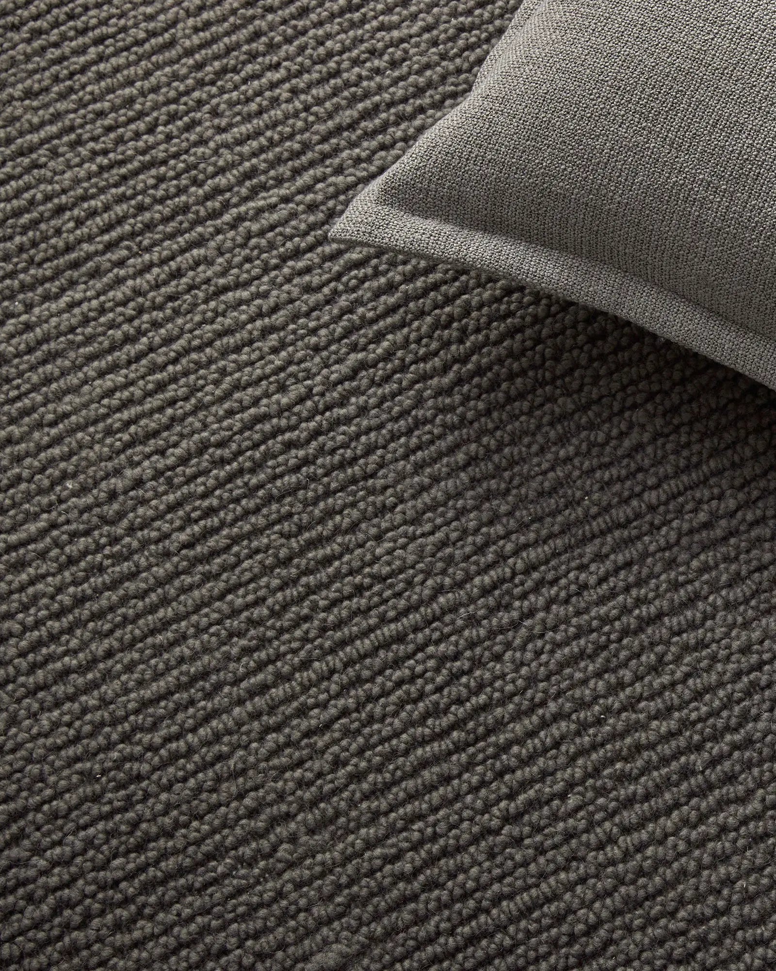 Layered neutral wool rugs in charcoal and fog grey tones, showcasing textured woven surfaces and subtle tonal variations in a minimalist interior styling