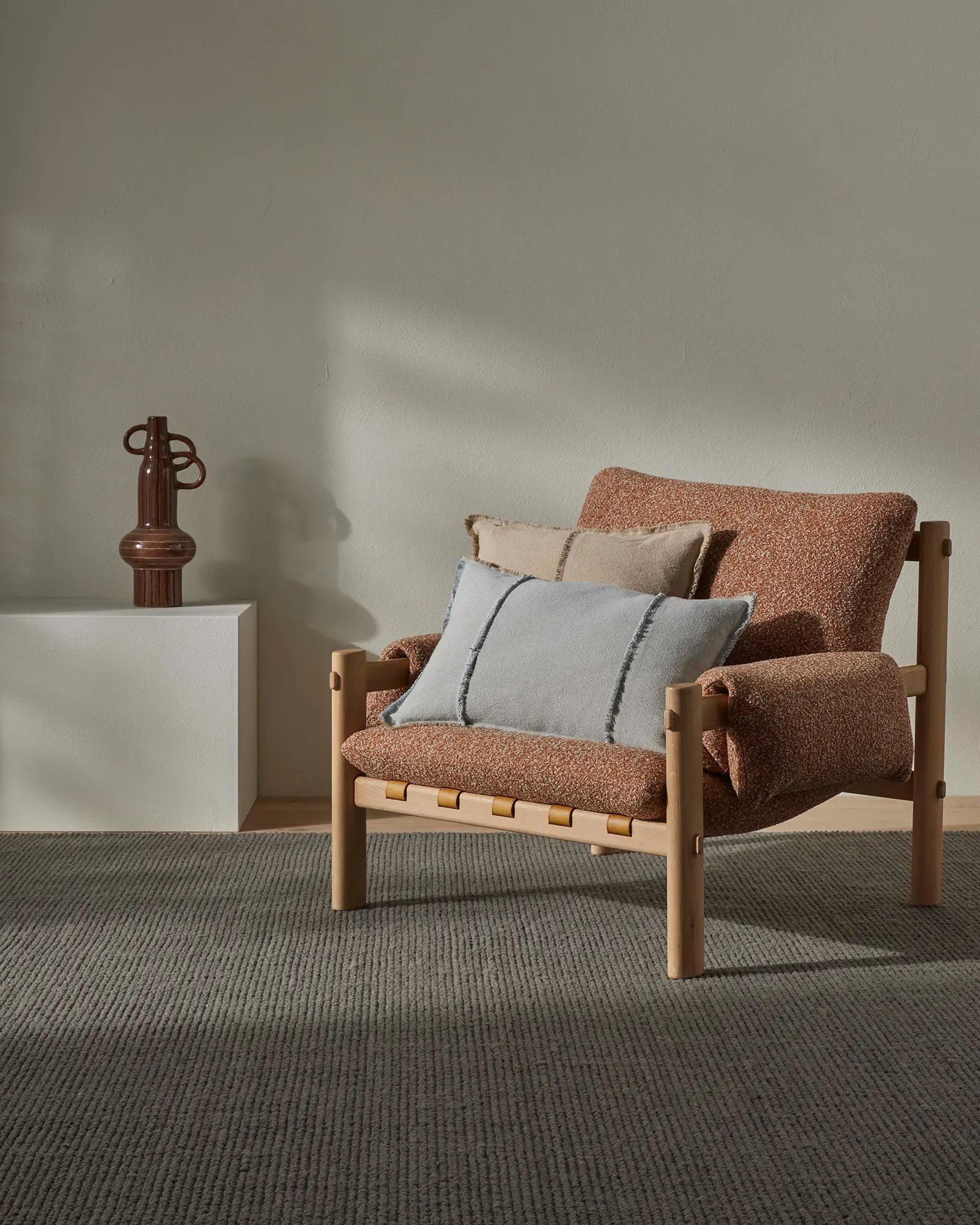 Mid-century wooden armchair layered with terracotta boucle textiles and pale blue accent cushions on textured sage wool rug, minimalist Scandinavian interior styling