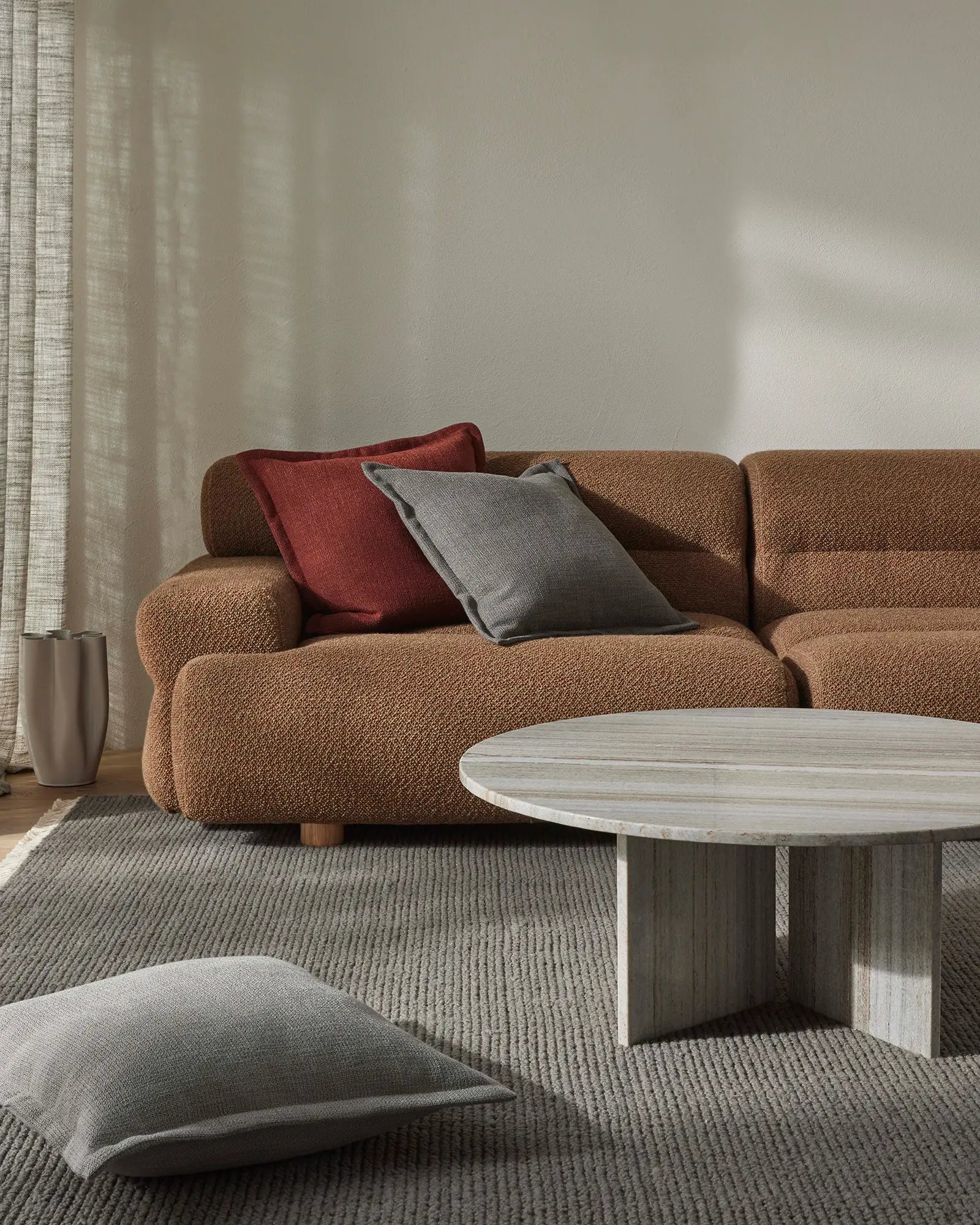 Warm minimalist living room with caramel linen sofa, layered Figlio cushions in paprika and graphite, grey wool rug, and soft natural light from linen curtains