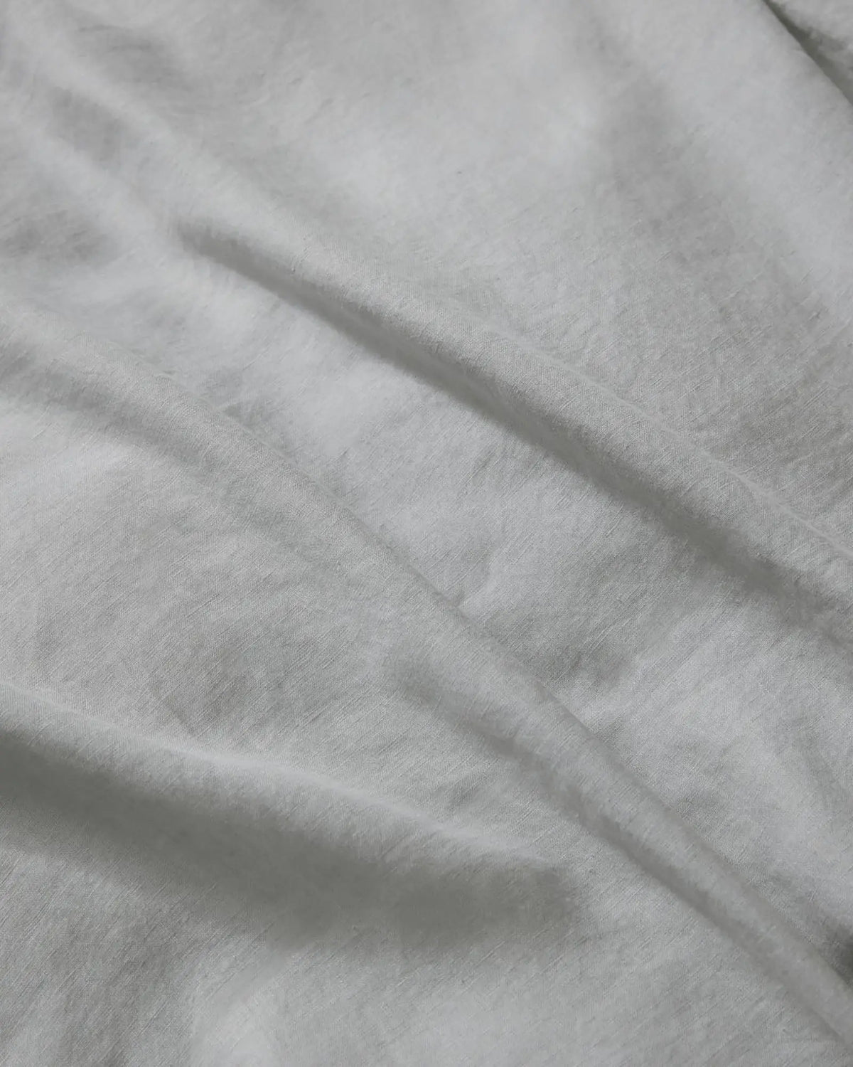 Close-up of silver Ravello flat sheet showing soft crumpled linen texture and natural light play on neutral bedding fabric